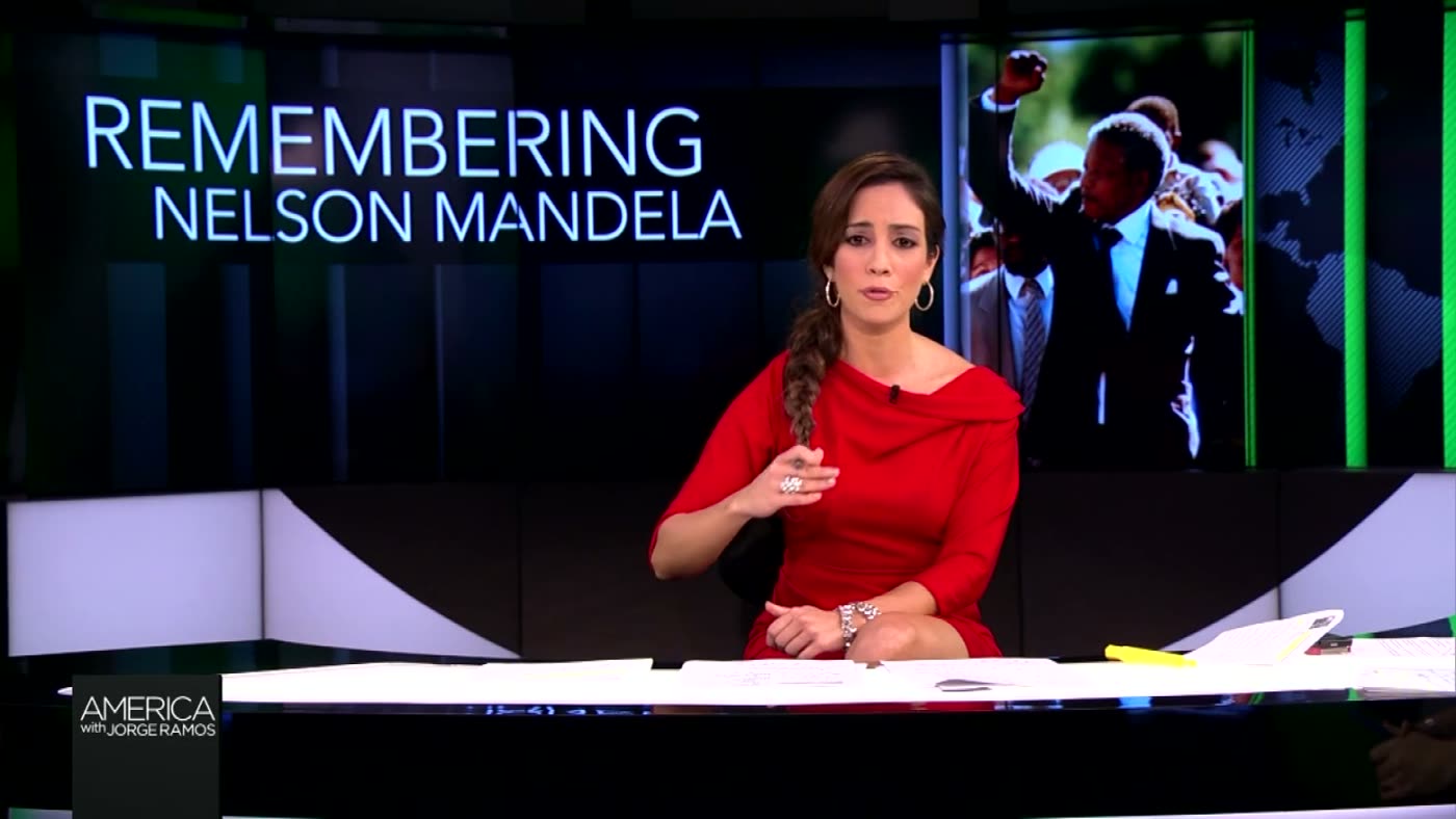 Mariana Atencio at the anchor desk with the Remembering Nelson Mandela board